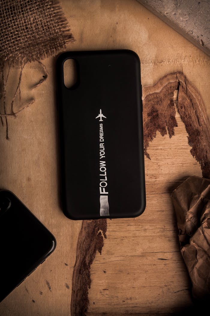Black phone case with 'Follow Your Dreams' message on rustic wooden table.